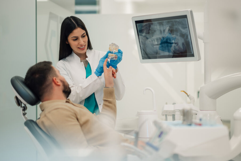 Female dentist showing teeth model to patient in modern clinic